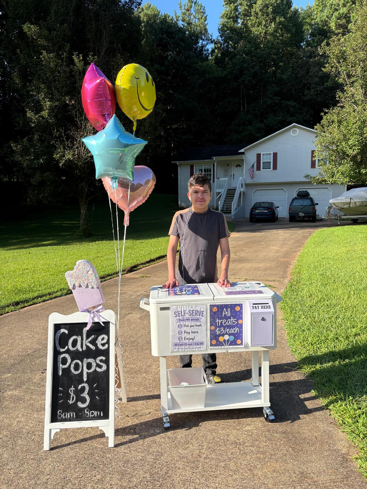 Mathias standing at his treat stand with balloons and a Cake Pops sign